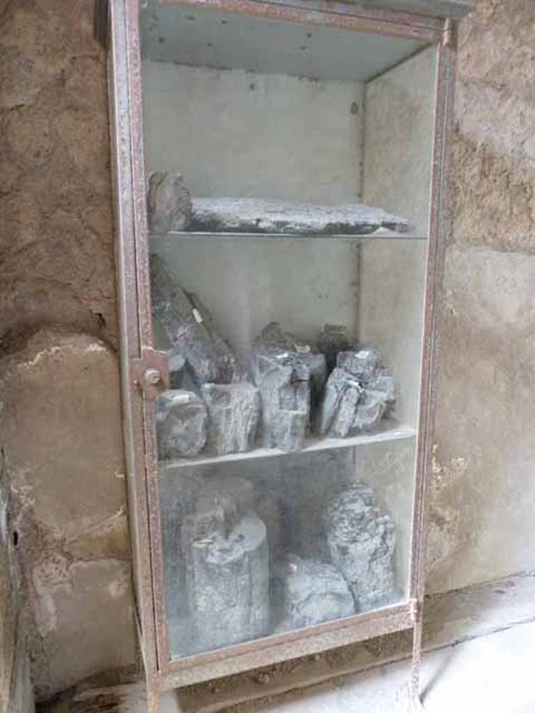 V 19, Herculaneum. May 2010. The glass show-case resting near the west wall contains some fragments of beams and carbonized wood.